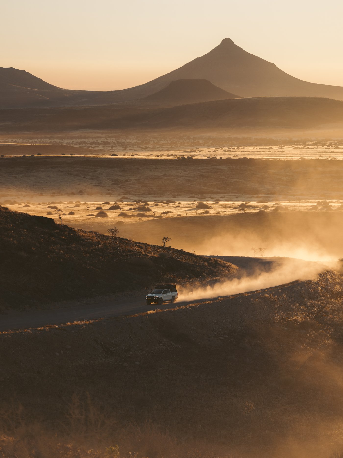 A 4x4 driving a dirt road through the Namibian desert at dusk, dust trailing behind