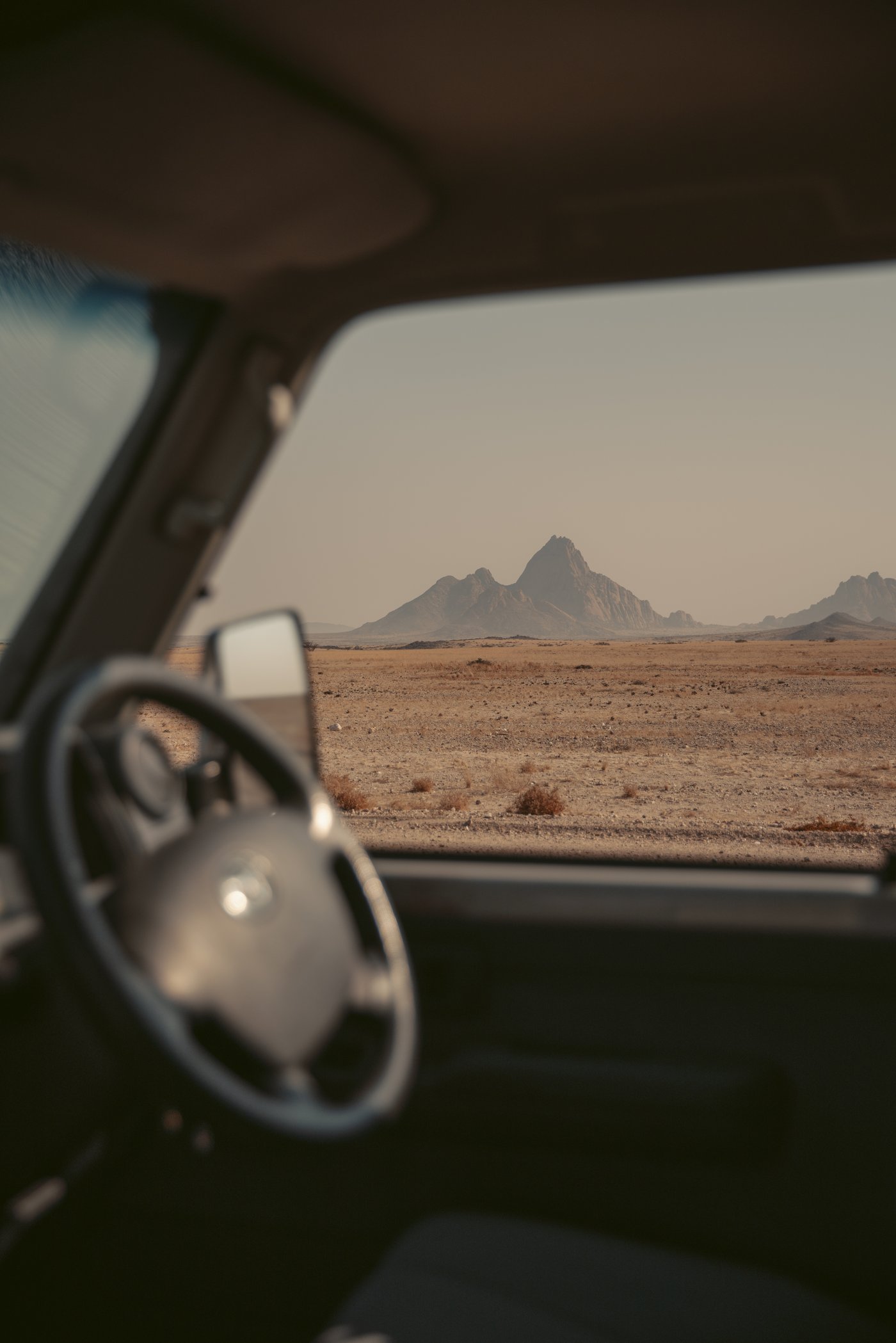 View through a car windshield of Spitzkoppe granite peak rising from the flat Namibian desert