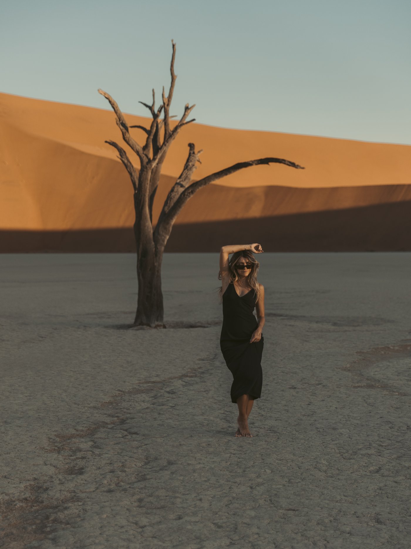 Emma standing in front of a dead acacia tree at Deadvlei with red dunes rising behind, Namibia
