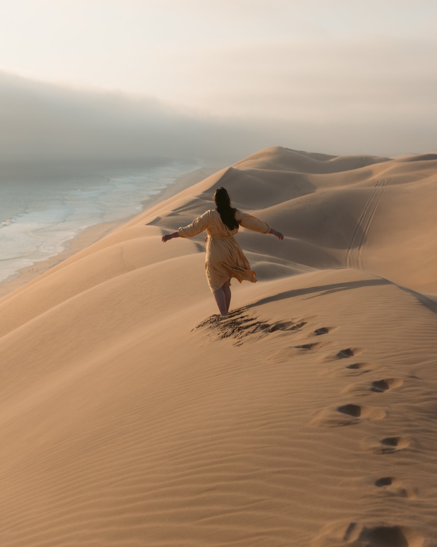 Emma standing on a coastal sand dune above the Atlantic Ocean near Swakopmund, Namibia, arms outstretched
